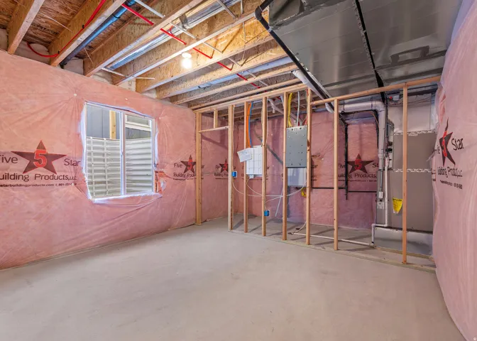 Unfinished lower level featuring an egress window, exposed wood ceiling joists, pink insulation, and framed interior walls