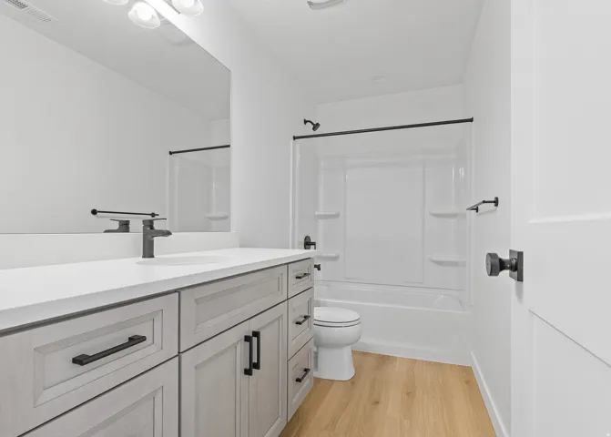 Contemporary bathroom featuring a light wood-finish vanity with matte black hardware, a white countertop, and an integrated sink