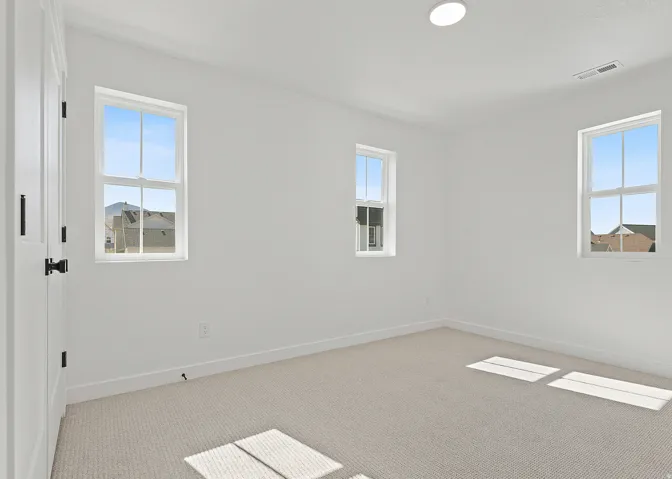 Carpeted room with white walls, three windows with white frames, white baseboards, and a flush-mount ceiling light