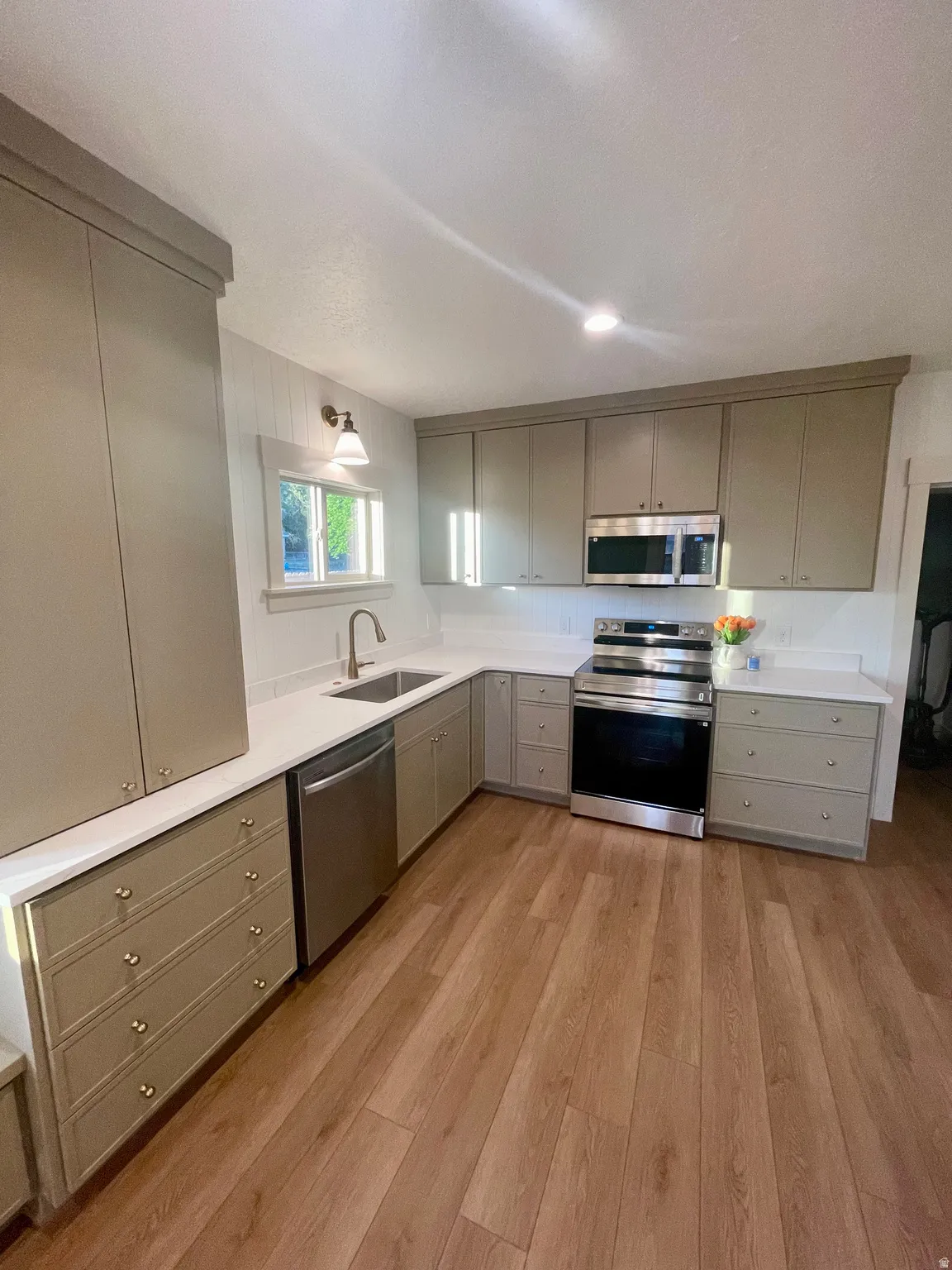 U-shaped kitchen featuring wood-finish flooring, light-toned cabinetry, white countertops, and stainless steel appliances, including a built-in microwave and dishwasher
