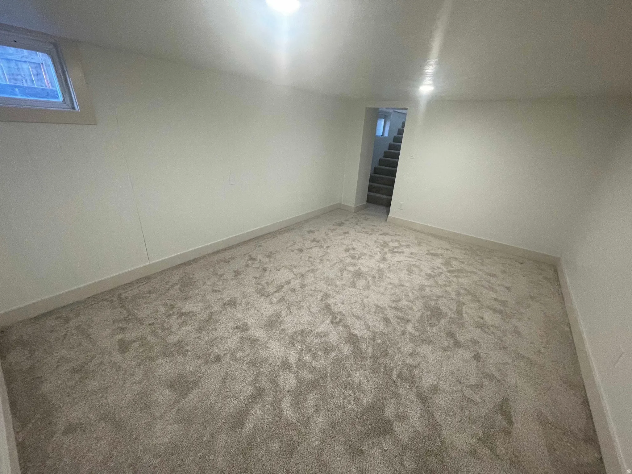 Finished basement area featuring plush gray carpeting, white painted walls, a single horizontal window, and recessed lighting