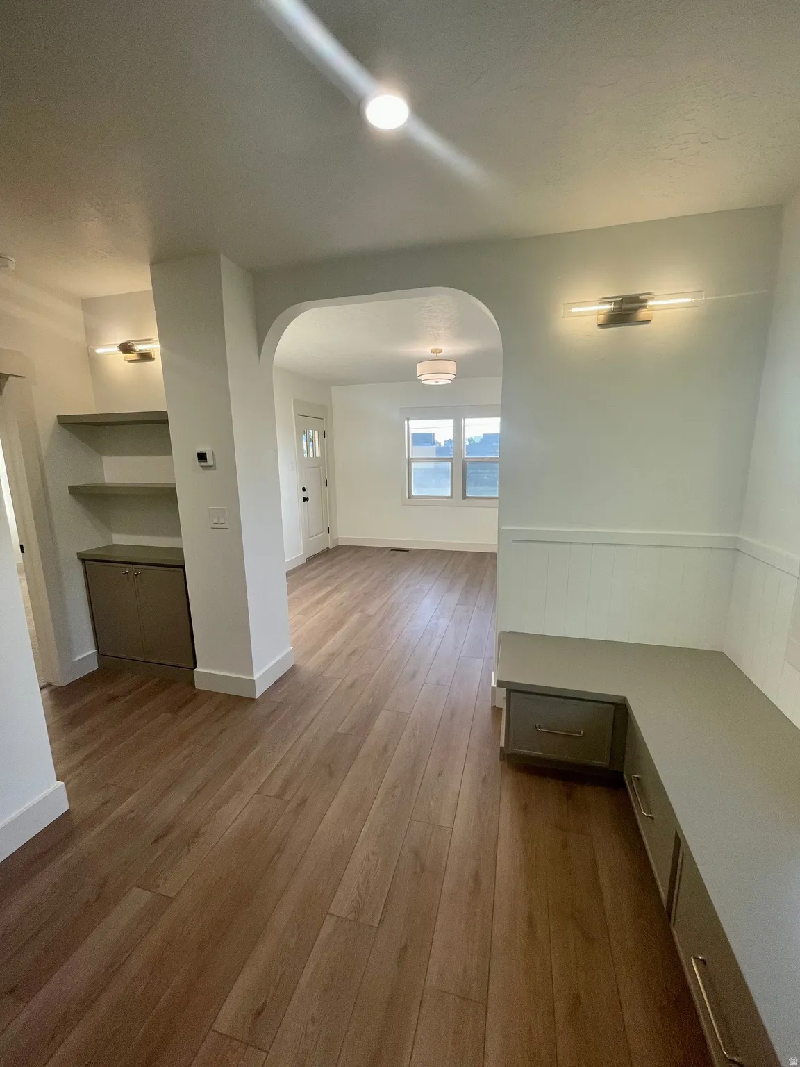 Entryway featuring wood-finish flooring, wainscoting, an arched doorway, built-in bench seating with storage, and recessed lighting