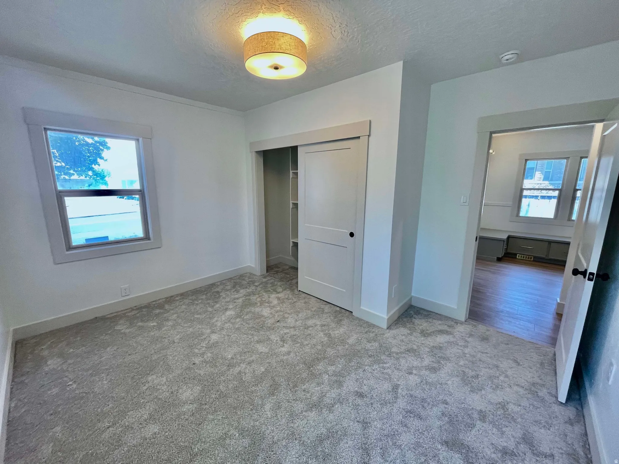 Neutral-toned room featuring a single window with white trim, light gray textured carpet, and a flush-mount ceiling light fixture