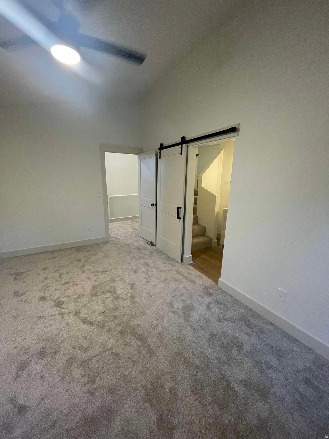 Spacious primary bedroom with vaulted ceiling and grey carpeting and barn door to primary bathroom