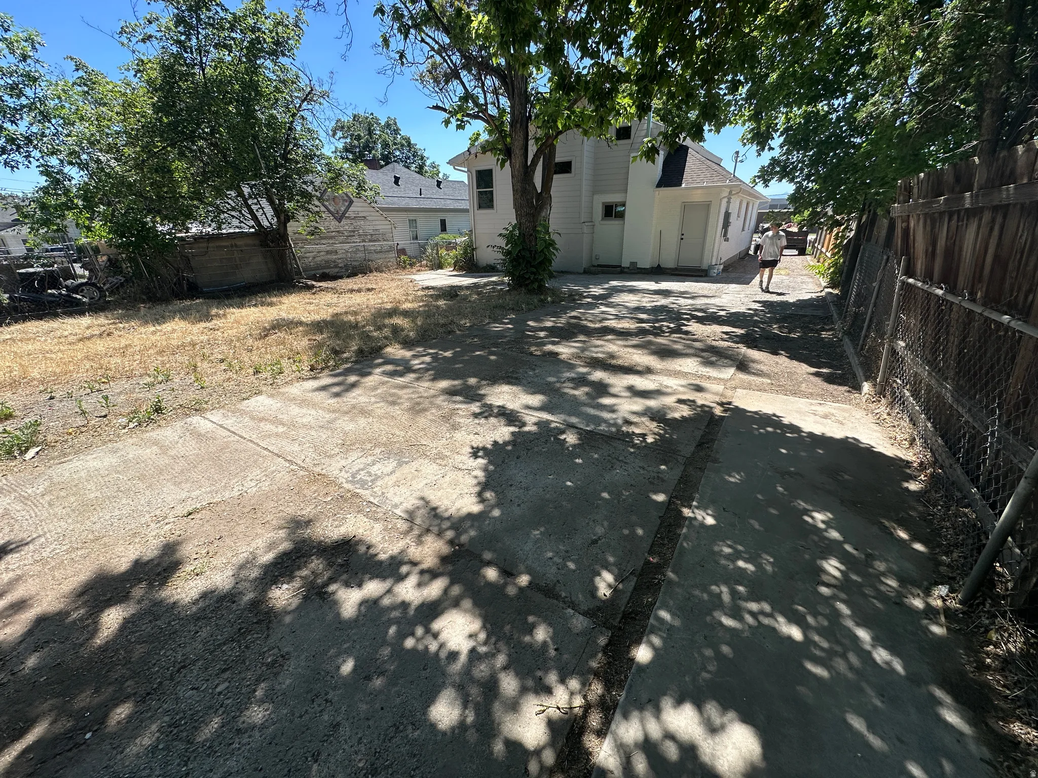 Paved driveway with a chain-link fence, mature trees, and a detached structure