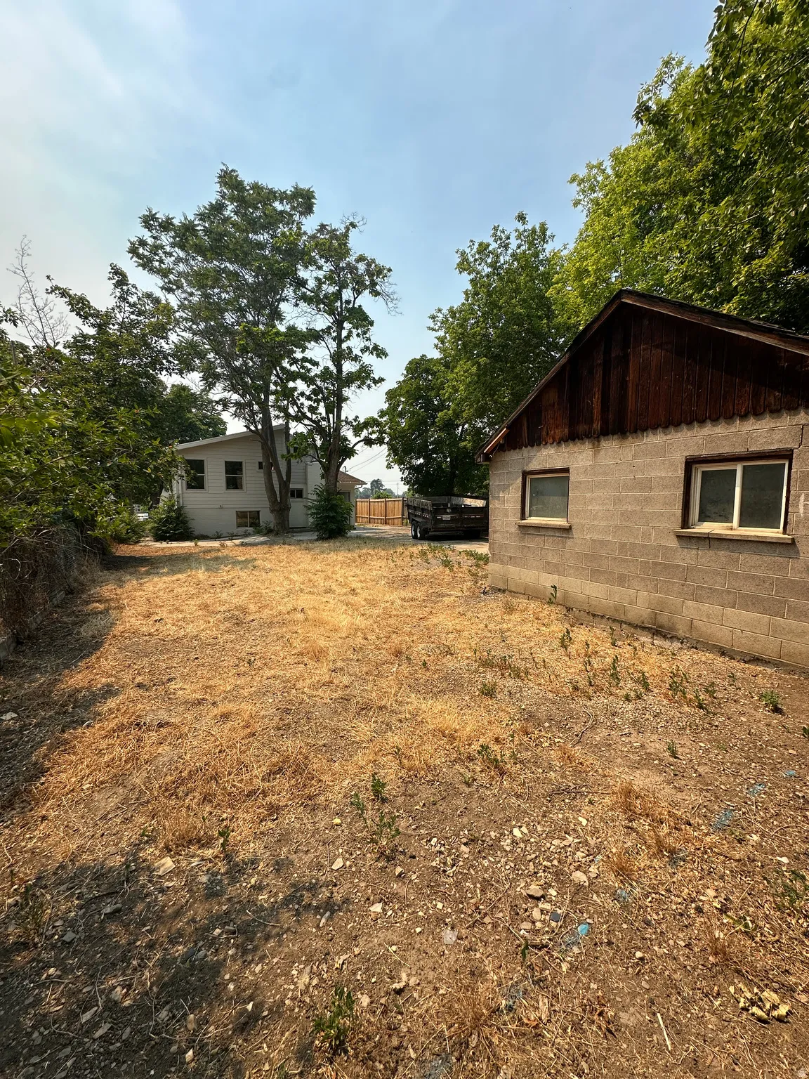 Expansive outdoor area featuring a concrete block structure with multiple windows, a wooden gable, and surrounding mature trees