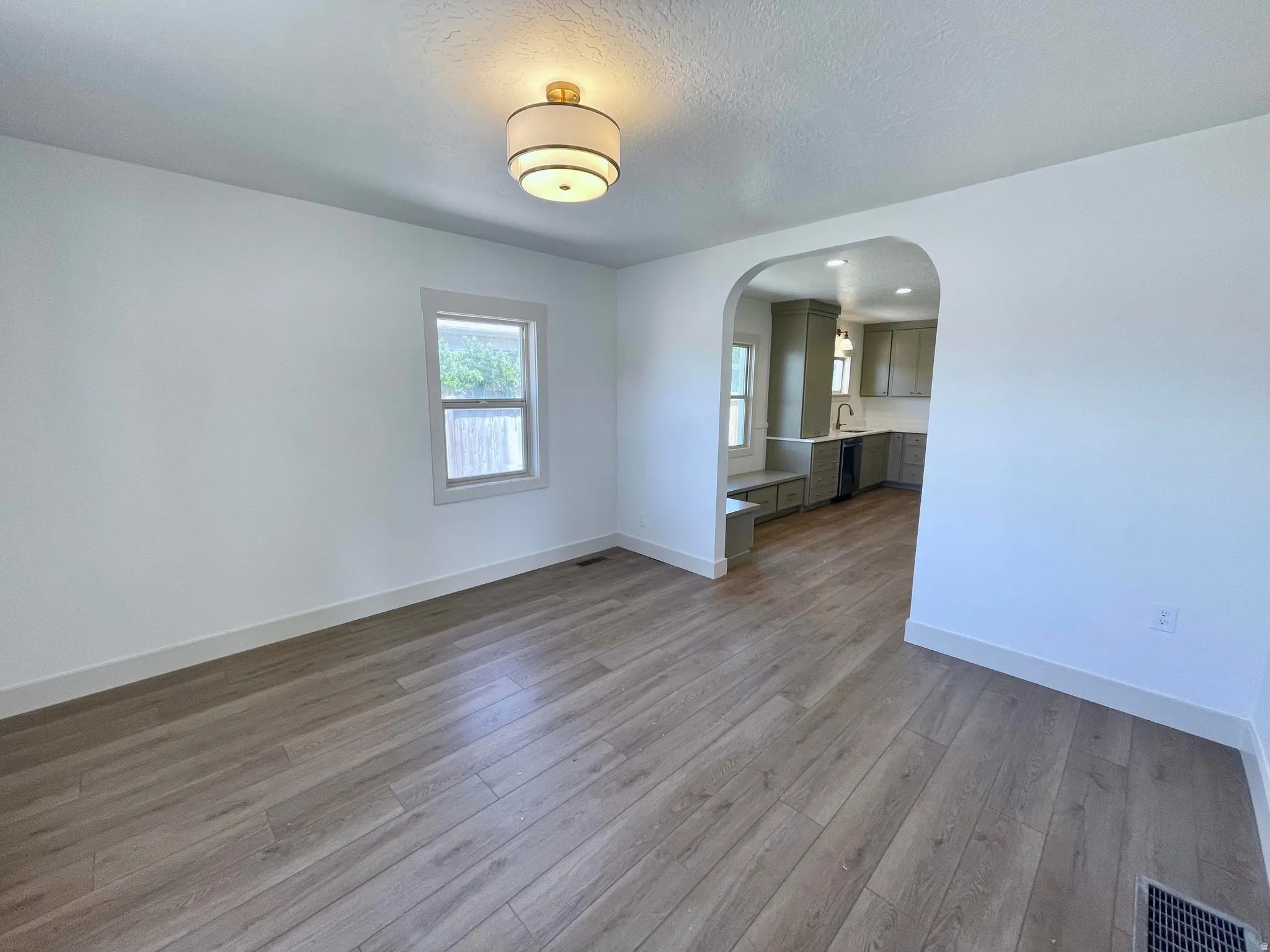Open interior featuring wood-finish flooring, a contemporary semi-flush mount light fixture, and an arched doorway leading to a kitchen with built-in cabinetry and a window