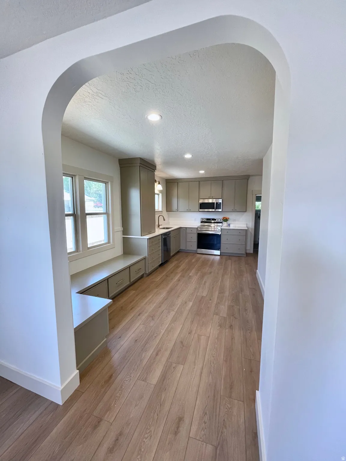 Open concept kitchen featuring wood-finish flooring, recessed lighting, built-in bench seating with storage, light gray cabinetry, and stainless steel appliances
