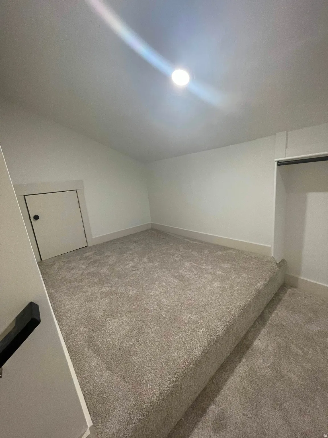 Carpeted interior space featuring an elevated platform, recessed lighting, a door with a black handle, and an open closet area