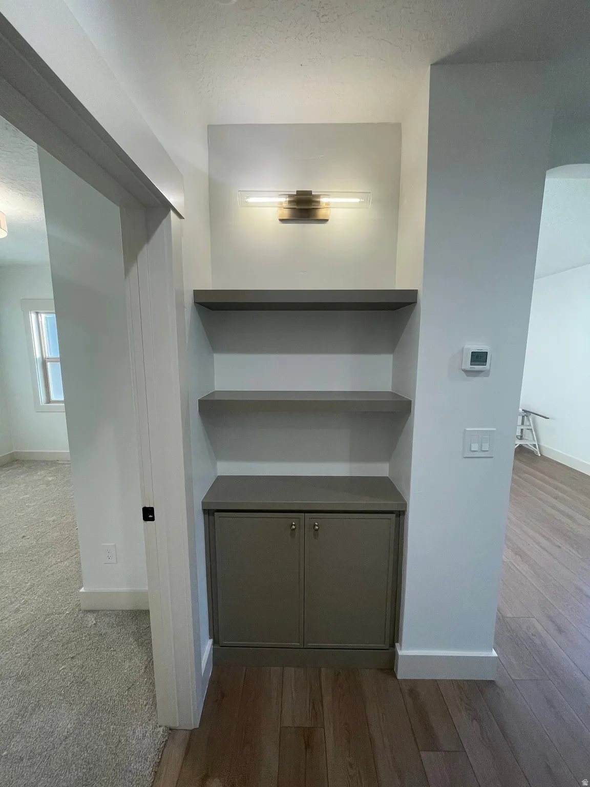Recessed built-in shelving unit featuring a two-door base cabinet, two open shelves, and an overhead linear light fixture