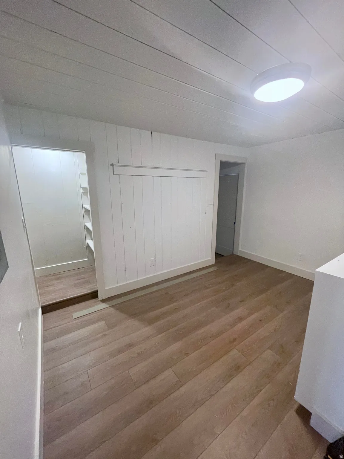 Room featuring wood-finish flooring, white shiplap ceiling, and white painted walls