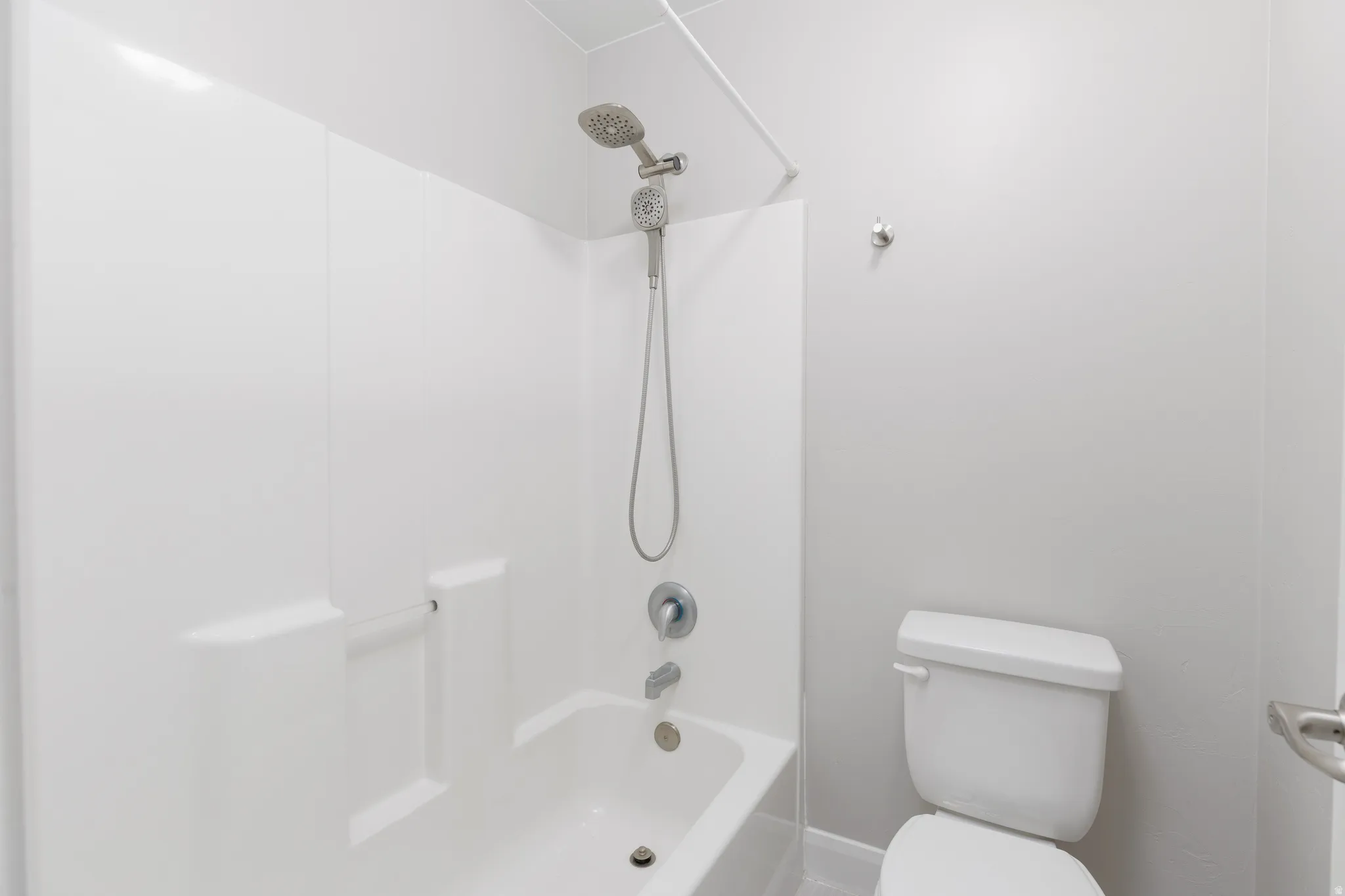 Bathroom featuring a white tub-shower combination with a textured surround, a dual shower head, and a white toilet
