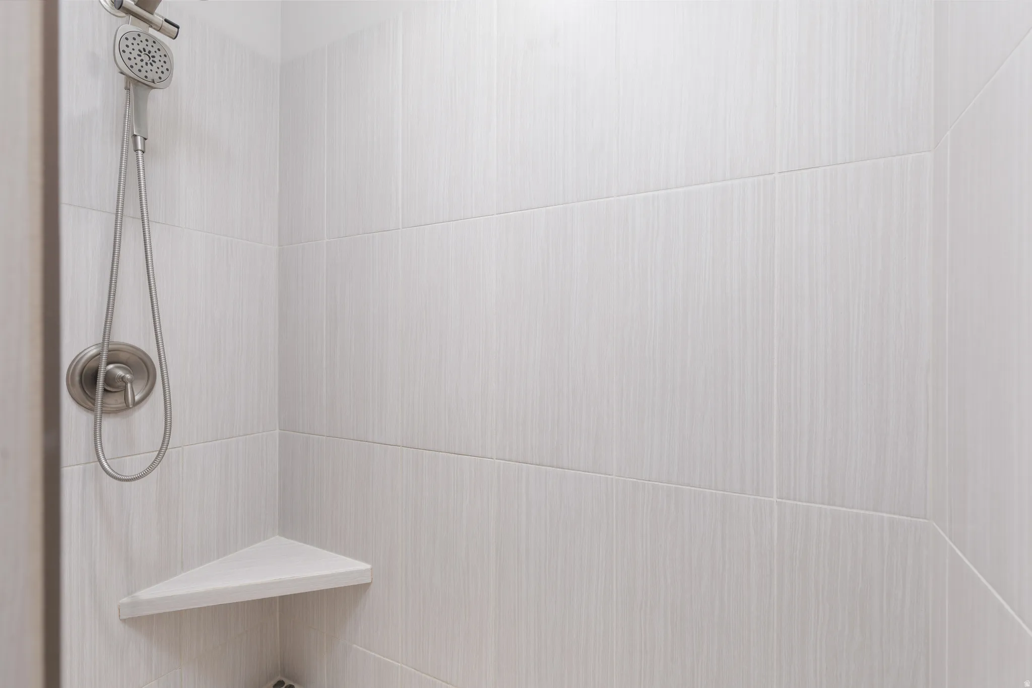 Shower stall featuring light-toned tilework with subtle vertical striations
