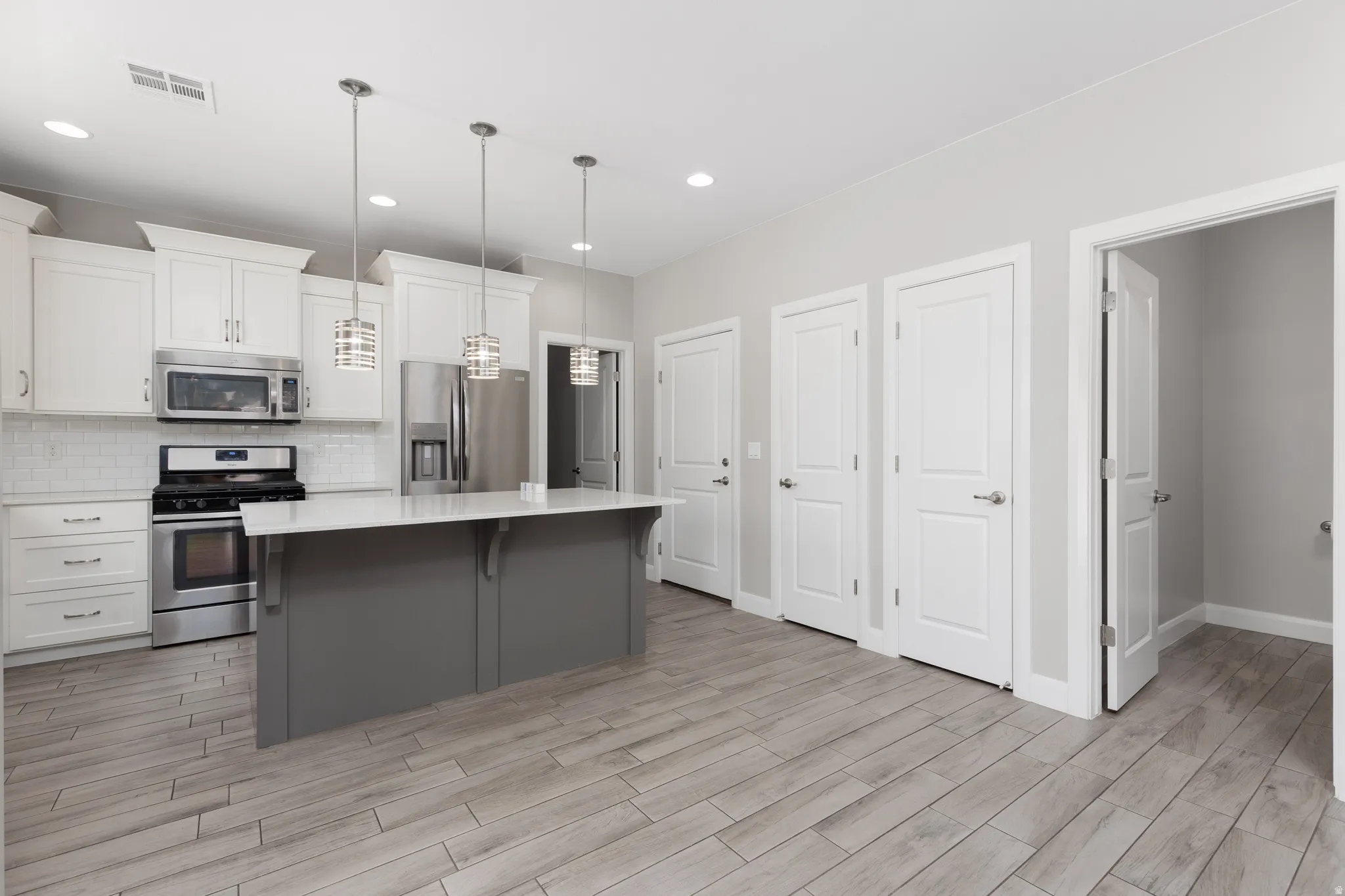 Modern kitchen featuring light wood-finish flooring, a central island with a white countertop, stainless steel appliances, white cabinetry, and recessed lighting