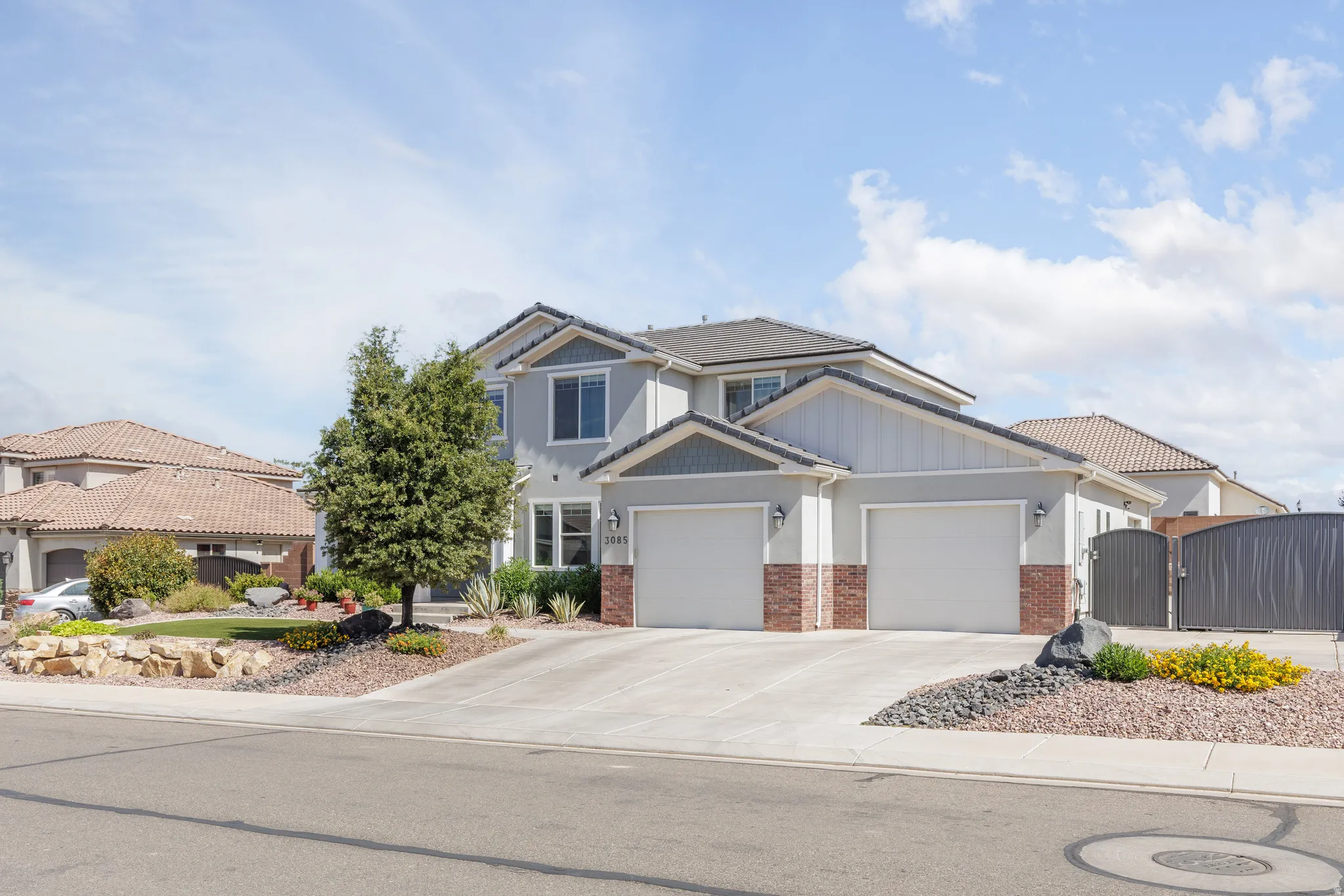Two-story residence featuring light gray siding with brick accents, a dark gray tiled roof, and a two-car garage