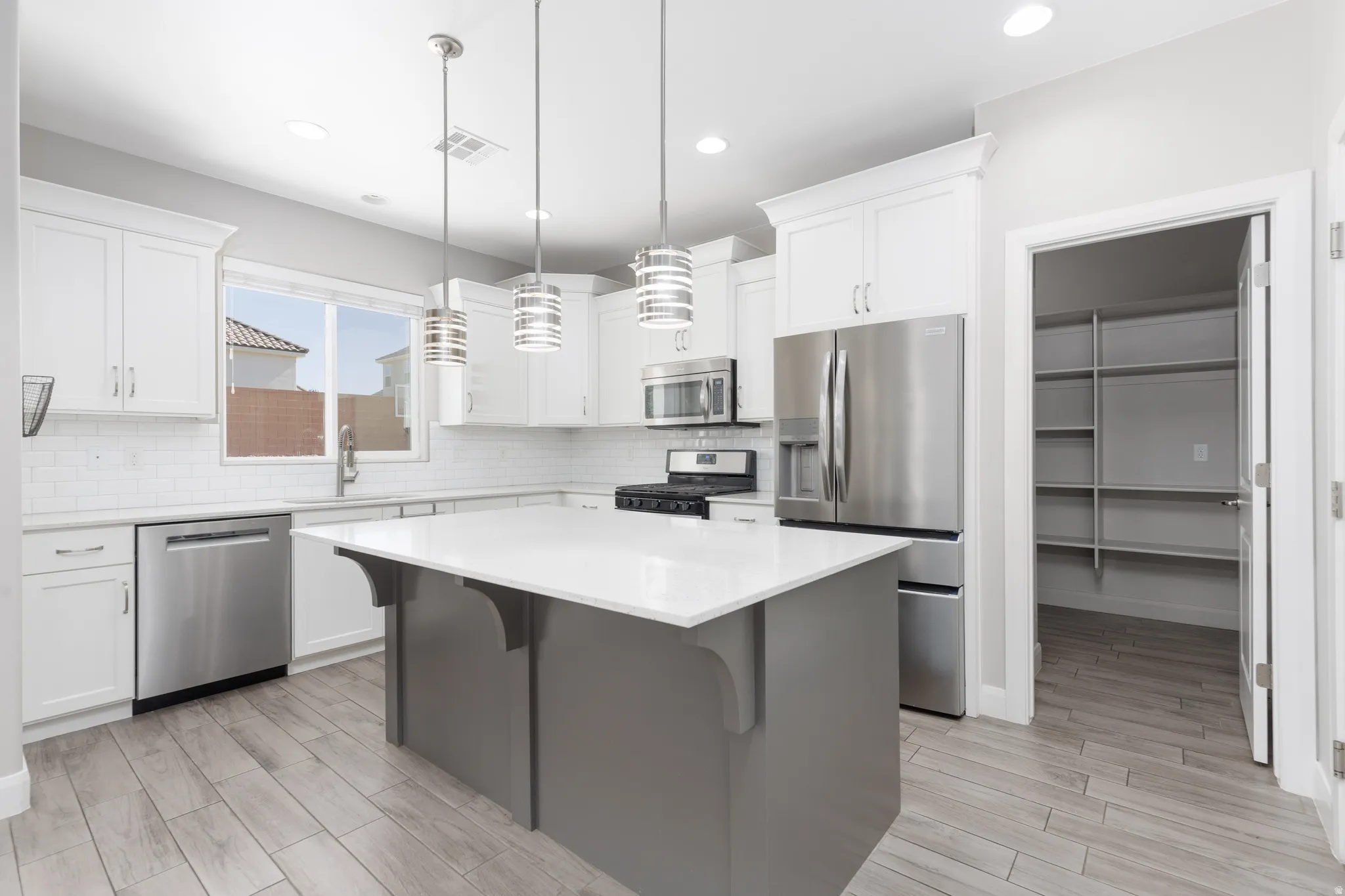 Modern kitchen featuring a central island with a white countertop, stainless steel appliances, white cabinetry, a subway tile backsplash, and wood-finish flooring
