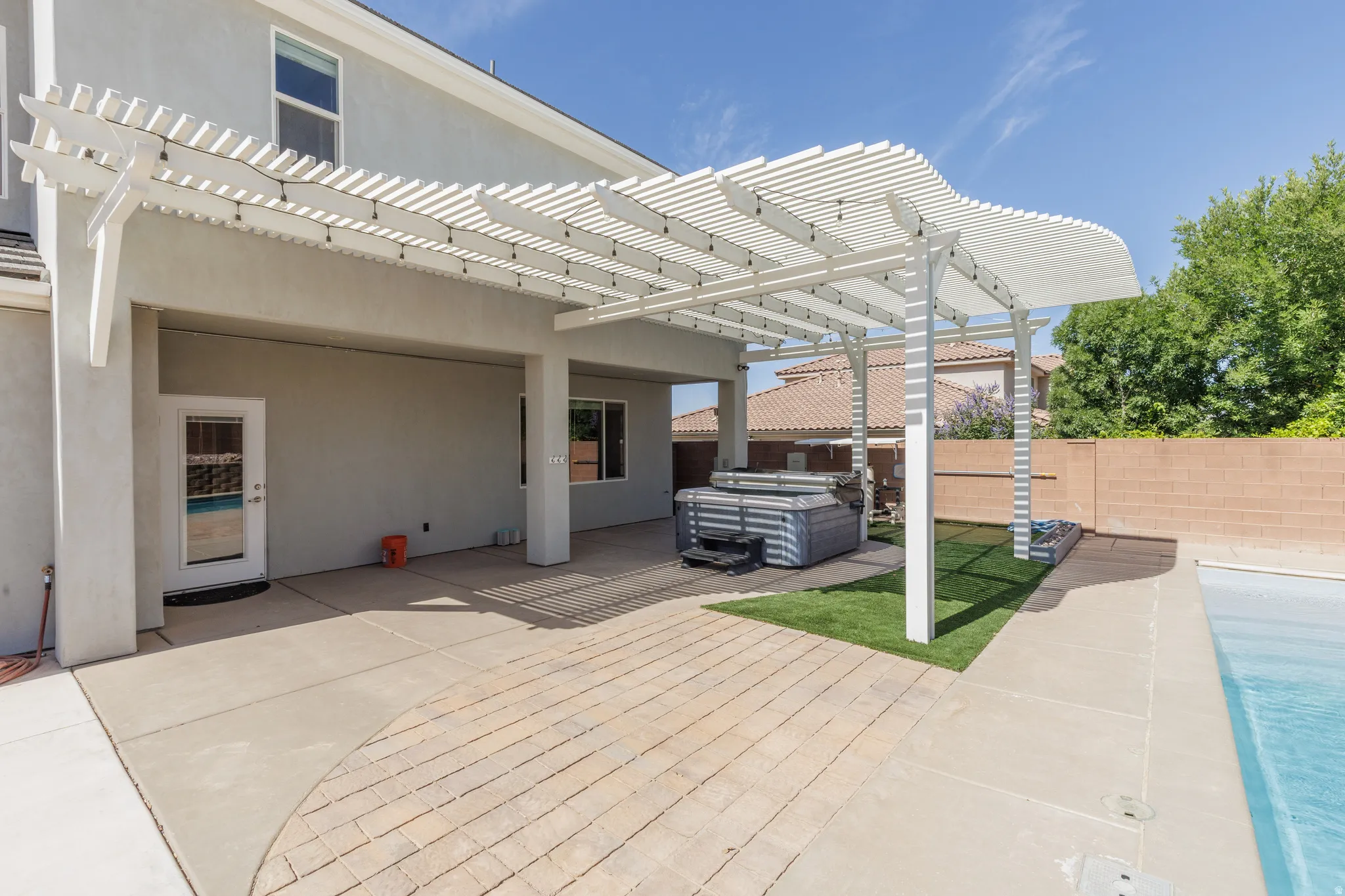 Backyard patio featuring a white slatted pergola with string lighting, a concrete patio area, and a patterned paver section