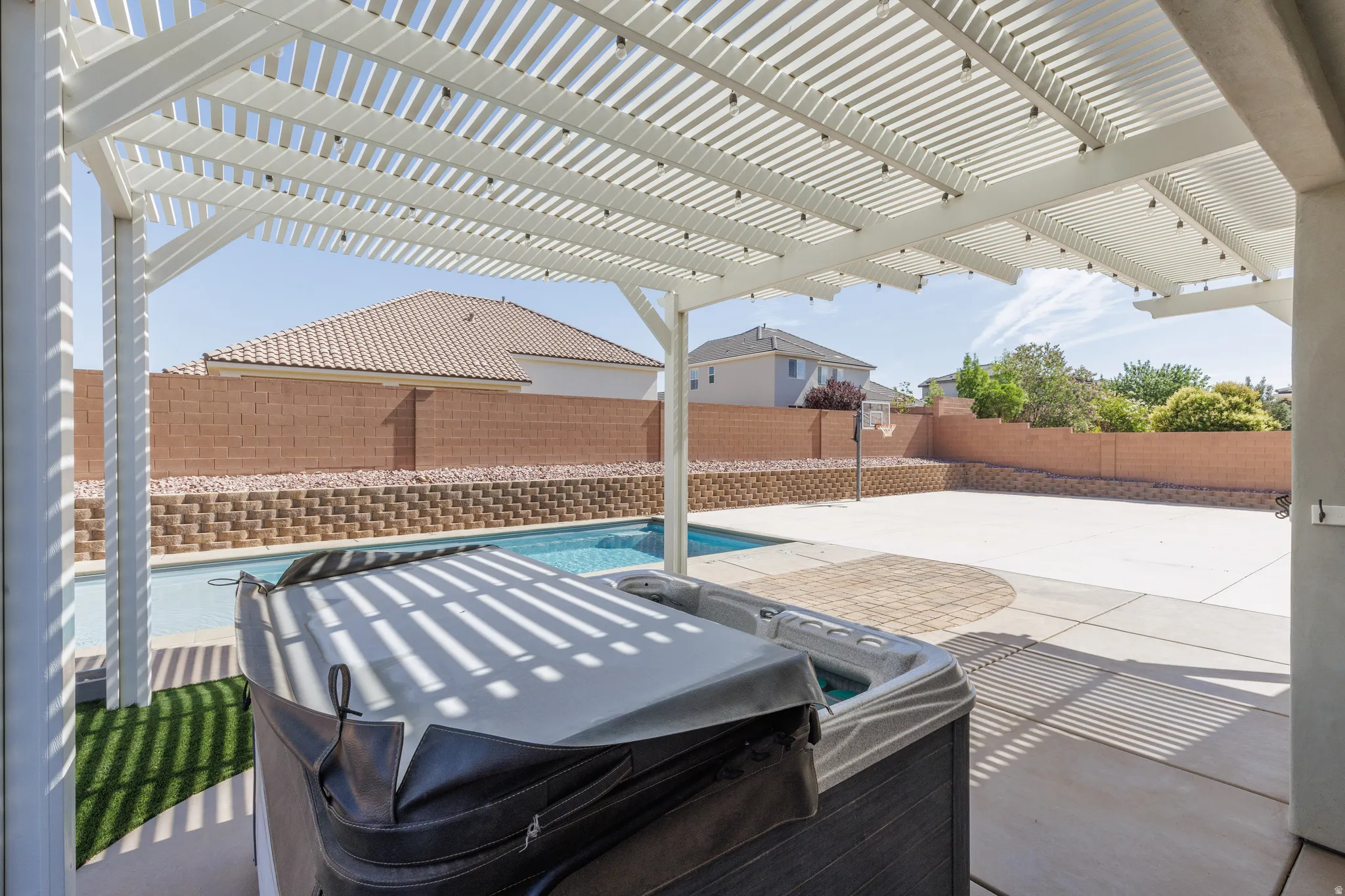 Expansive outdoor living area featuring a white slatted pergola, a built-in swimming pool, a hot tub, and a spacious concrete patio