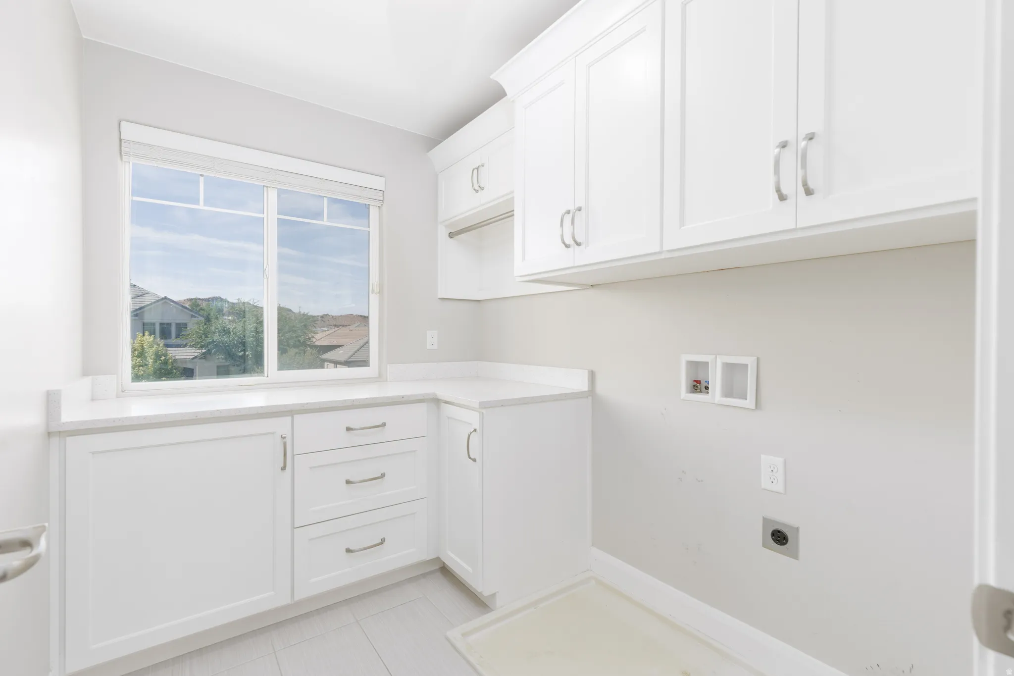Laundry room featuring white cabinetry, light-toned countertops, and a window