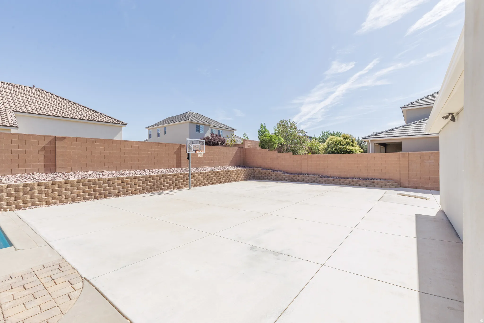 Expansive backyard featuring a large concrete patio, a basketball hoop, and a perimeter block wall