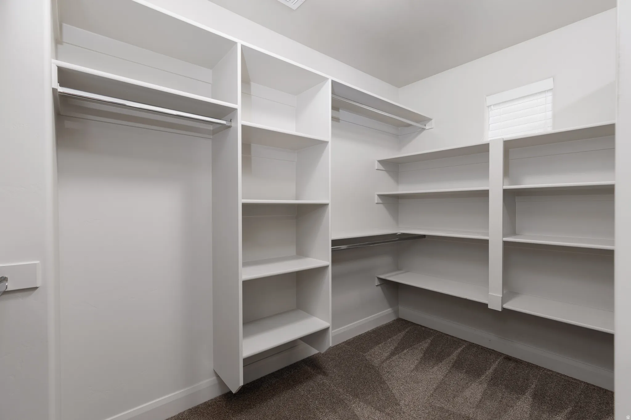 Walk-in closet featuring built-in white shelving, multiple hanging rods, and textured carpet flooring