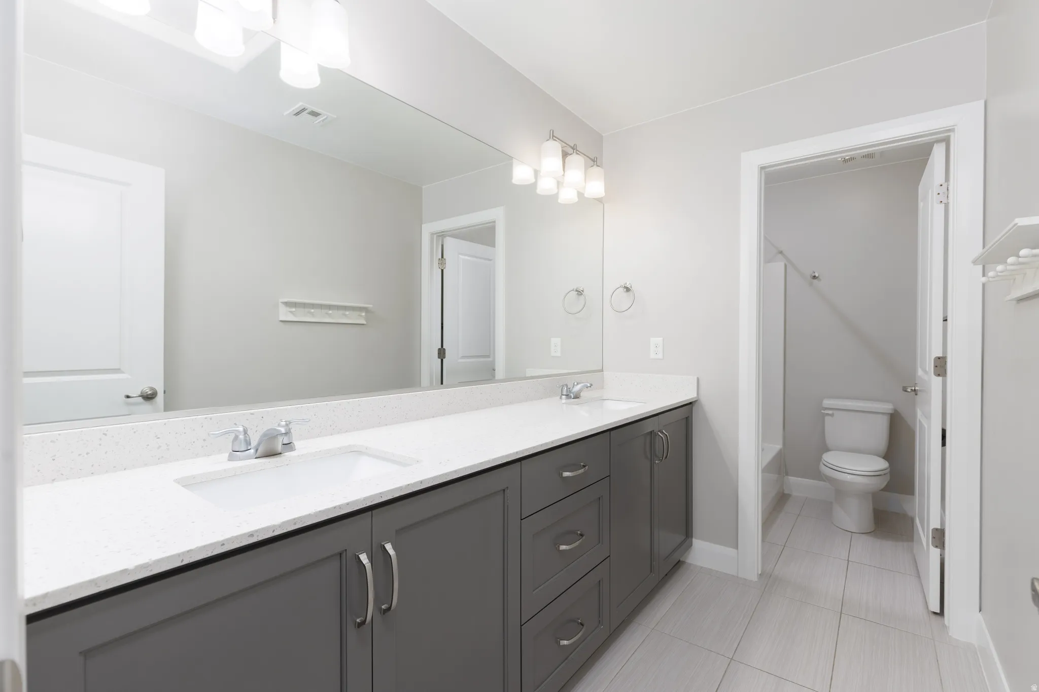 Spacious bathroom featuring a dual vanity with a white composite countertop, undermount sinks, and gray cabinetry with brushed nickel hardware
