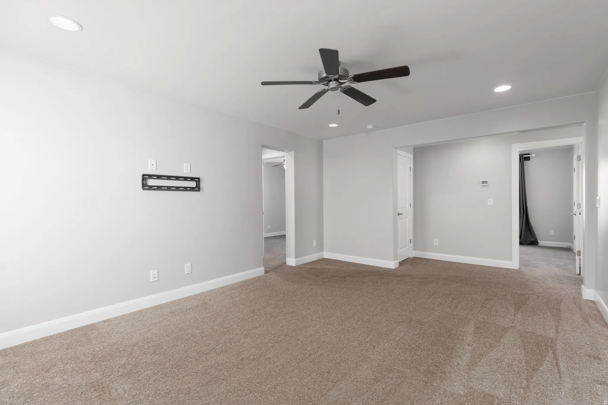 Carpeted interior space featuring light grey walls, white trim, recessed lighting, and a ceiling fan