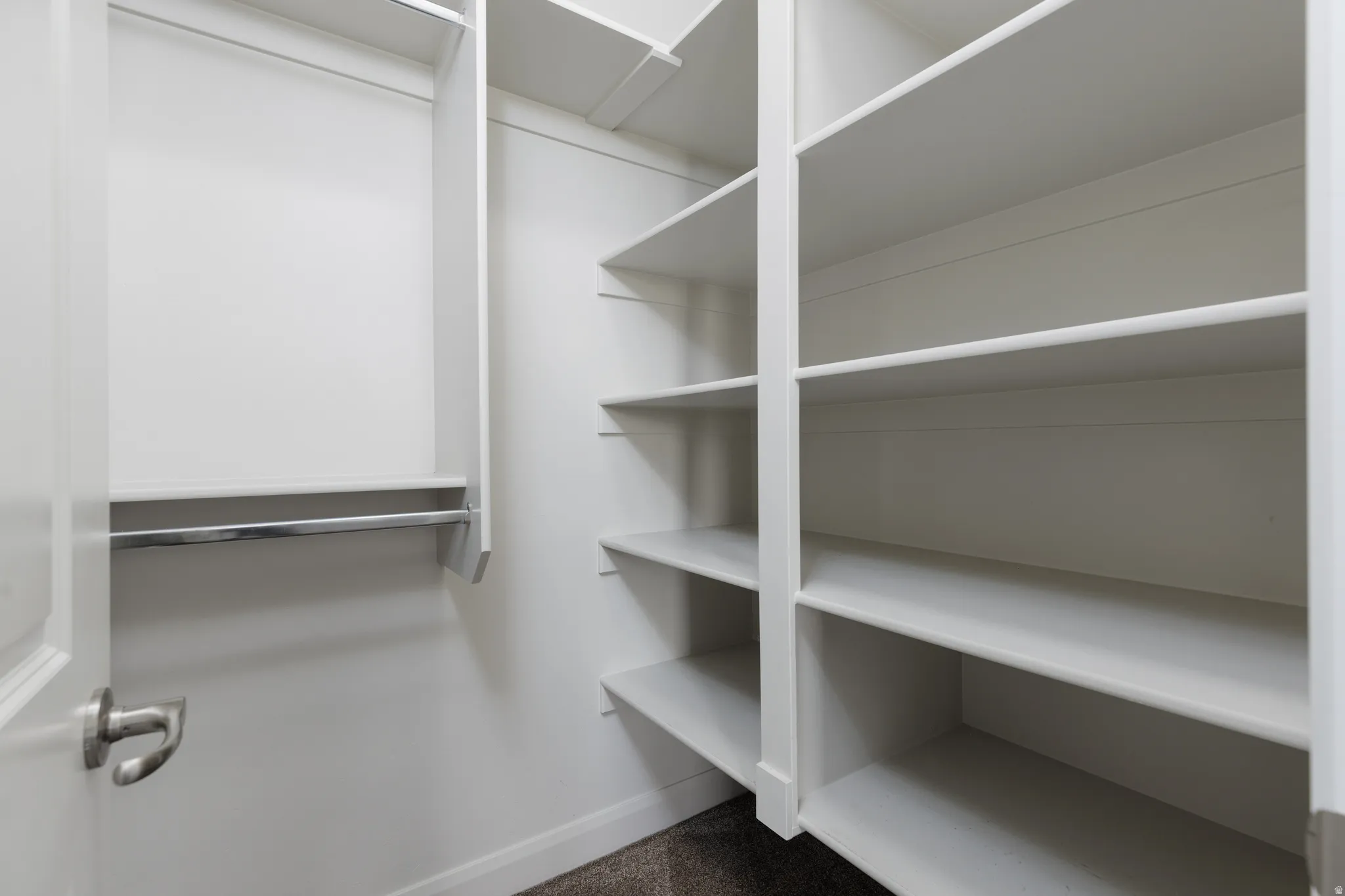 Walk-in closet featuring white built-in shelving, a chrome hanging rod, and white painted walls