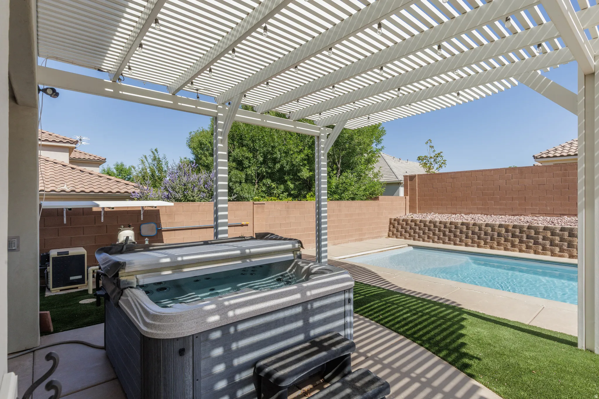Outdoor living area featuring a white slatted patio cover with string lighting, a built-in hot tub, an in-ground swimming pool, and artificial turf landscaping