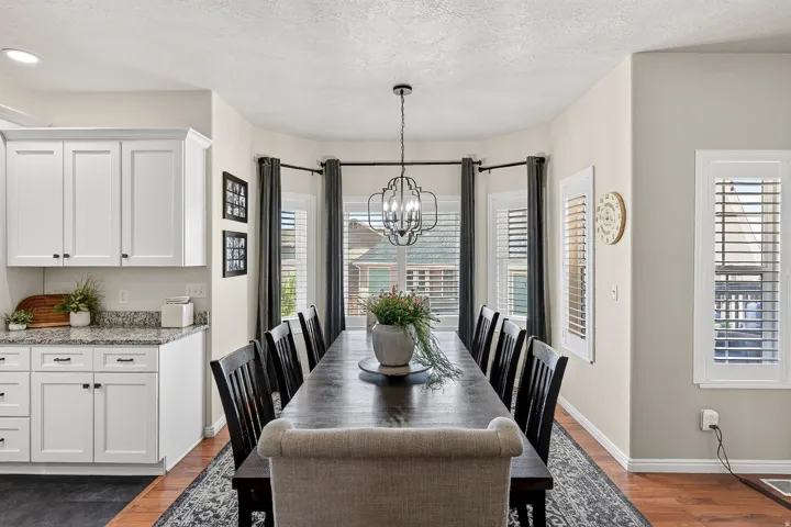 Dining area featuring a dark wood-finish table with seating for eight, a bay window with plantation shutters, and an overhead chandelier