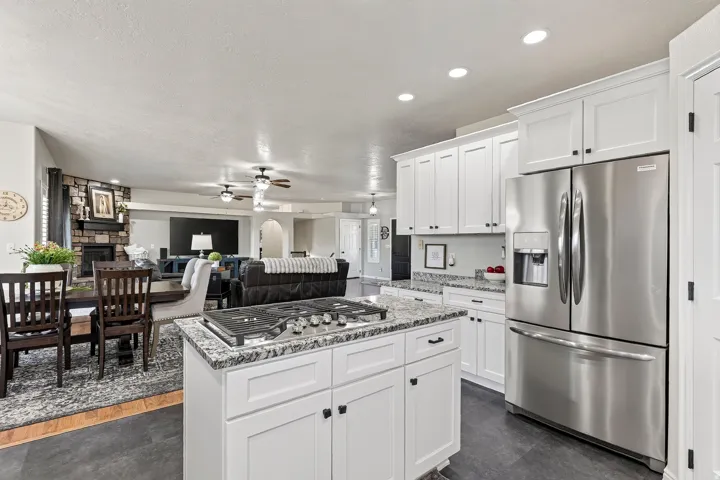 Contemporary kitchen featuring white cabinetry, stainless steel French door refrigerator, and a kitchen island with a gas cooktop and stone-finish countertop