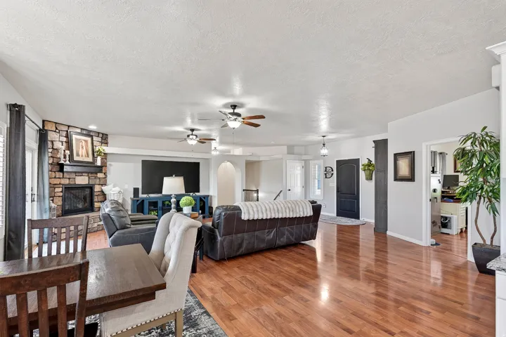 Spacious living area featuring wood-finish flooring, a stone-clad fireplace with a mantel, and multiple ceiling fans