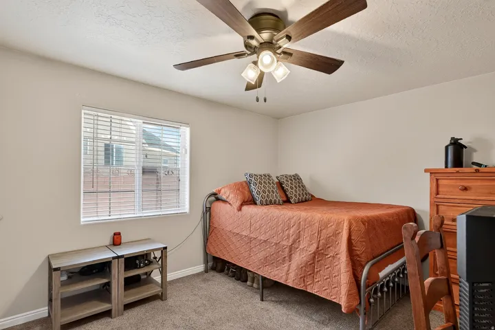 Neutral wall paint, textured ceiling, a window with horizontal blinds, carpeted flooring, and a ceiling fan with integrated lighting