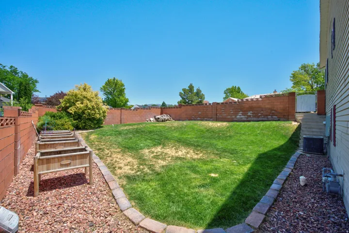 Expansive backyard featuring a manicured lawn, a full brick perimeter wall, and a side yard with raised garden beds