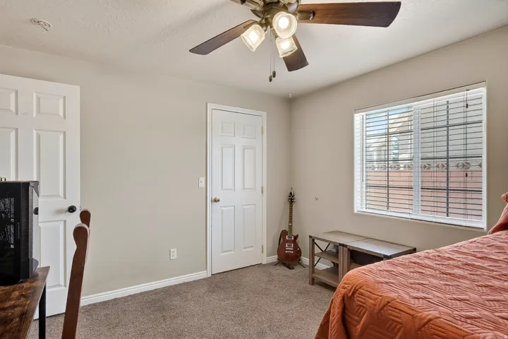 Carpeted room featuring a ceiling fan with light fixture, two paneled doors, and a window with horizontal blinds