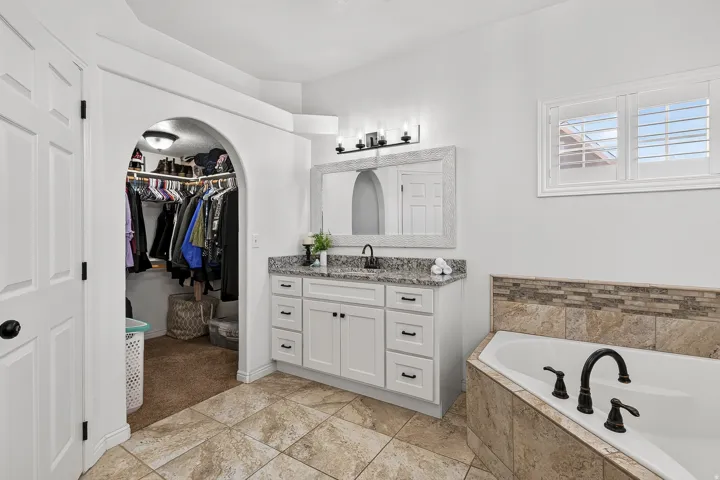 Bathroom featuring a single vanity with stone countertop, white cabinetry, and a framed mirror
