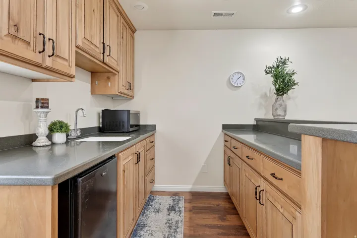 Kitchenette featuring wood-finish cabinetry with dark hardware, a stainless steel sink, a compact refrigerator, and ample countertop space