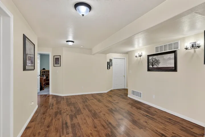 Spacious room featuring wood-finish flooring, light neutral wall paint, and multiple ceiling and wall-mounted light fixtures