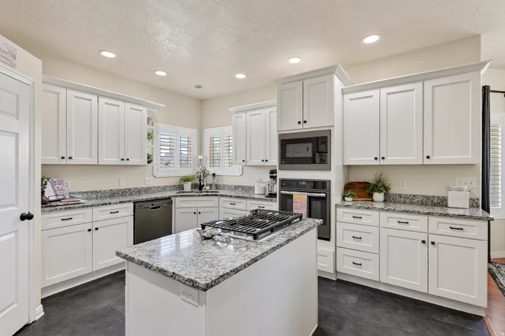Kitchen featuring white shaker-style cabinetry, granite countertops, a central island with a gas range, stainless steel appliances, and recessed lighting