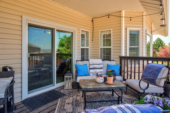 Covered deck featuring wood-finish decking, tan siding, multiple windows with white frames, and a sliding glass door