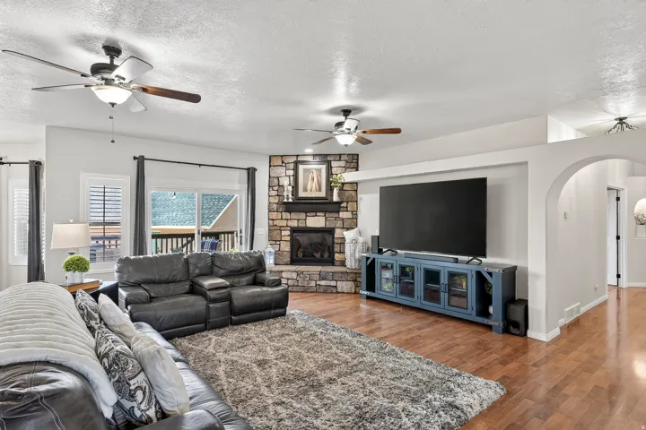 Spacious living area featuring wood-finish flooring, a corner-stacked stone fireplace, and ceiling fans