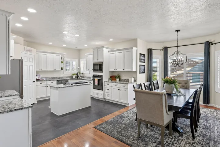 Open-concept kitchen and dining area featuring white cabinetry, granite countertops, an island with additional counter space, recessed lighting, and wood-finish flooring transitioning to tile