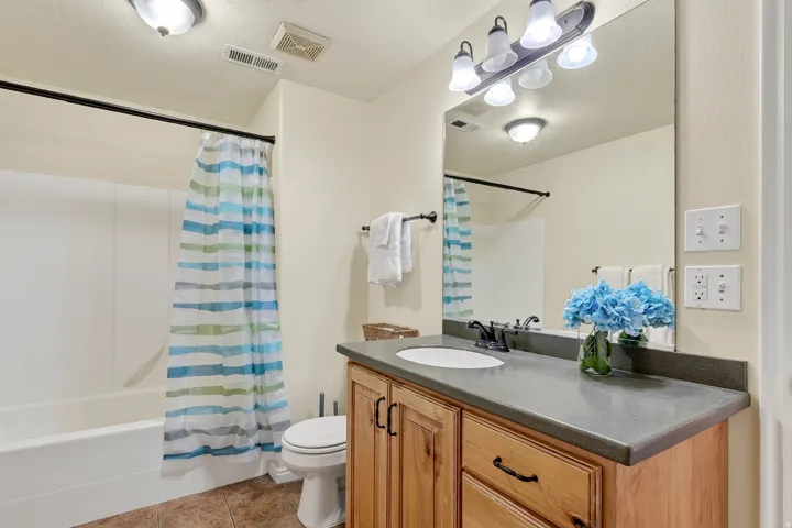 Bathroom featuring a white tub and shower combination, a wooden vanity with a built-in sink, a large wall-mounted mirror, and tile flooring