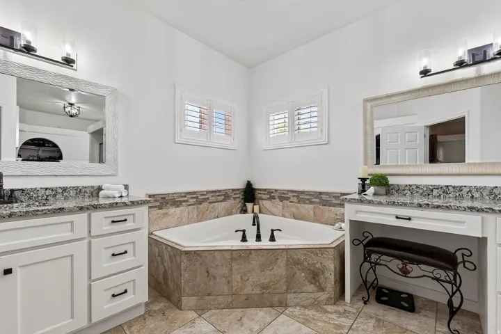 Corner soaking tub with a tiled surround, framed by white plantation shutters
