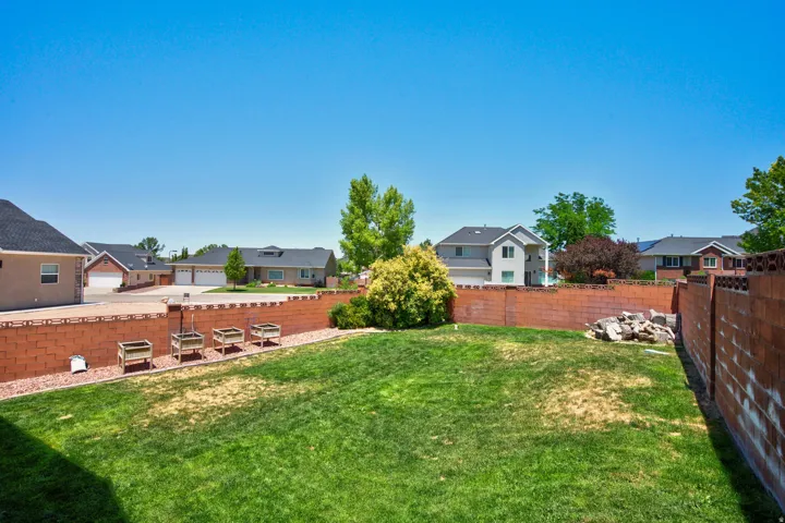 Expansive backyard featuring a manicured lawn, brick perimeter fencing, and raised garden beds