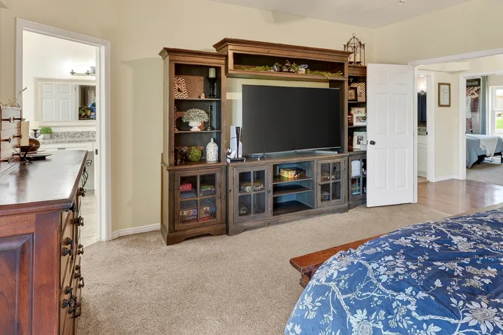 Neutral wall paint and carpeted flooring define this room, featuring a built-in entertainment center with open shelving and glass-front cabinets