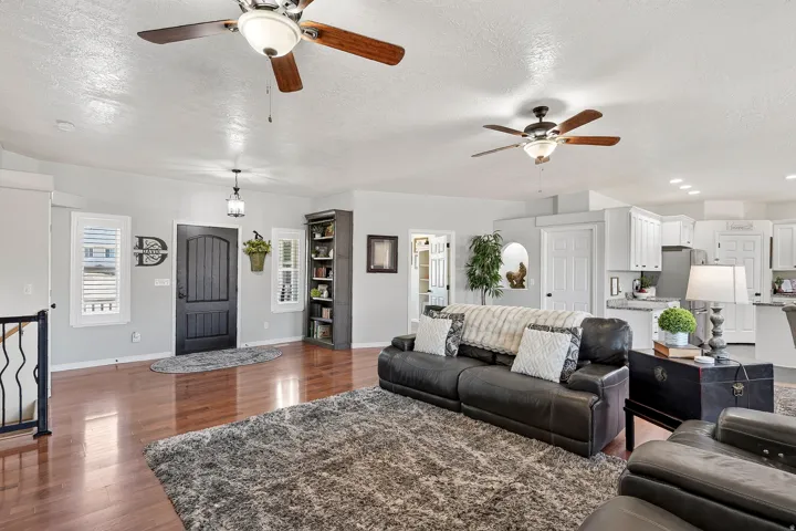 Spacious living area featuring warm wood-finish flooring, recessed lighting, and multiple ceiling fans