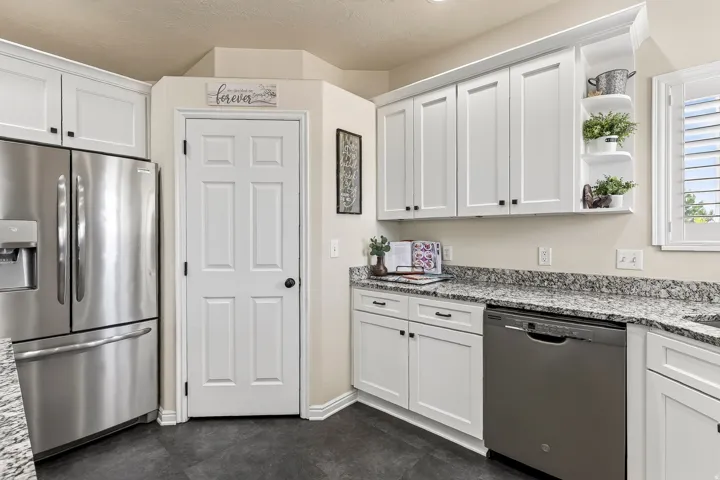 Kitchen featuring white shaker-style cabinetry, dark speckled countertops, and stainless-steel appliances including a refrigerator and dishwasher