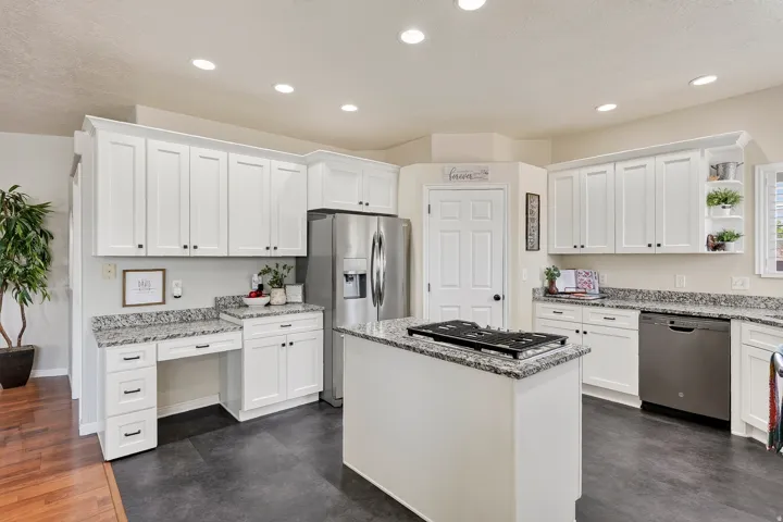 Modern kitchen featuring white shaker cabinetry, speckled countertops, stainless steel appliances, a center island with a cooktop, and recessed lighting