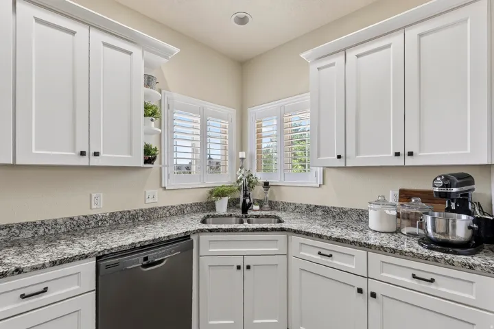 Kitchen featuring white shaker-style cabinetry with crown molding, stainless steel sink, granite countertops, and a built-in dishwasher